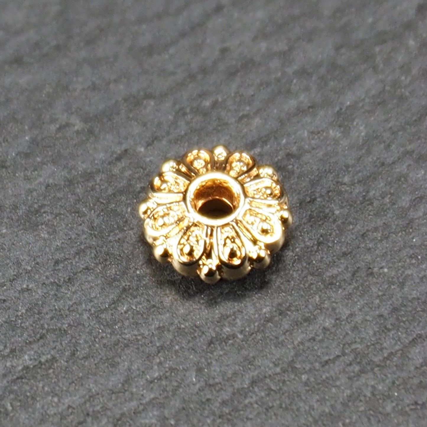 Runde, goldfarbene Scheiben-Spacer-Perle mit mittigem Loch und reliefierter, blütenartiger radialer Ornamentgravur.