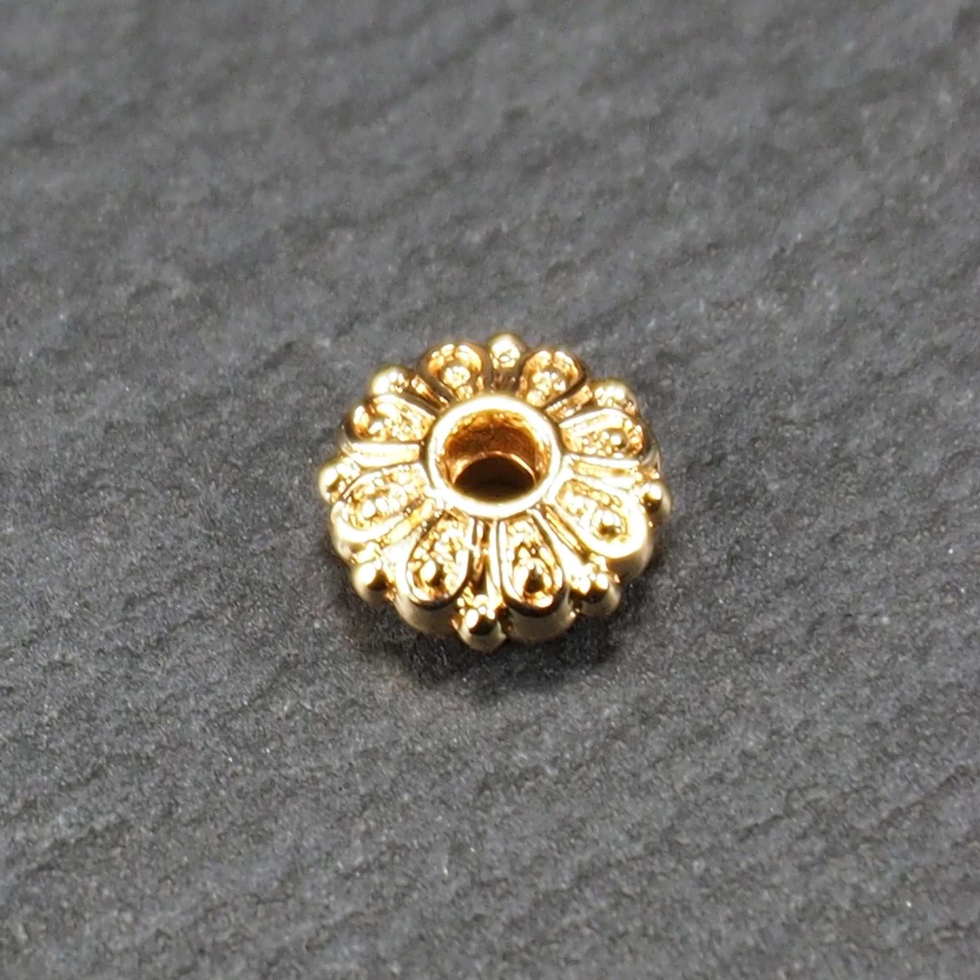 Runde, goldfarbene Scheiben-Spacer-Perle mit mittigem Loch und reliefierter, blütenartiger radialer Ornamentgravur.