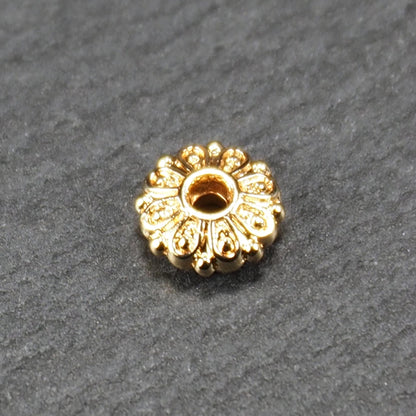 Runde, goldfarbene Scheiben-Spacer-Perle mit mittigem Loch und reliefierter, blütenartiger radialer Ornamentgravur.