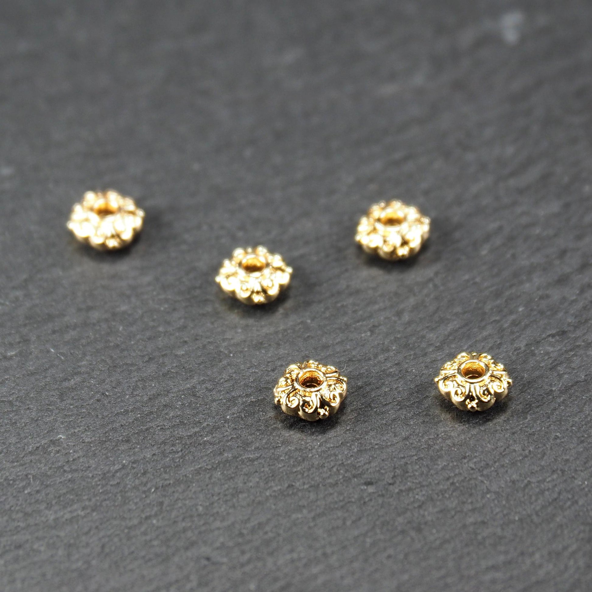 Runde goldfarbene Spacer Perlen mit glänzender Oberfläche, reliefartigem floralem Ornament und zentralem runden Durchbruch.