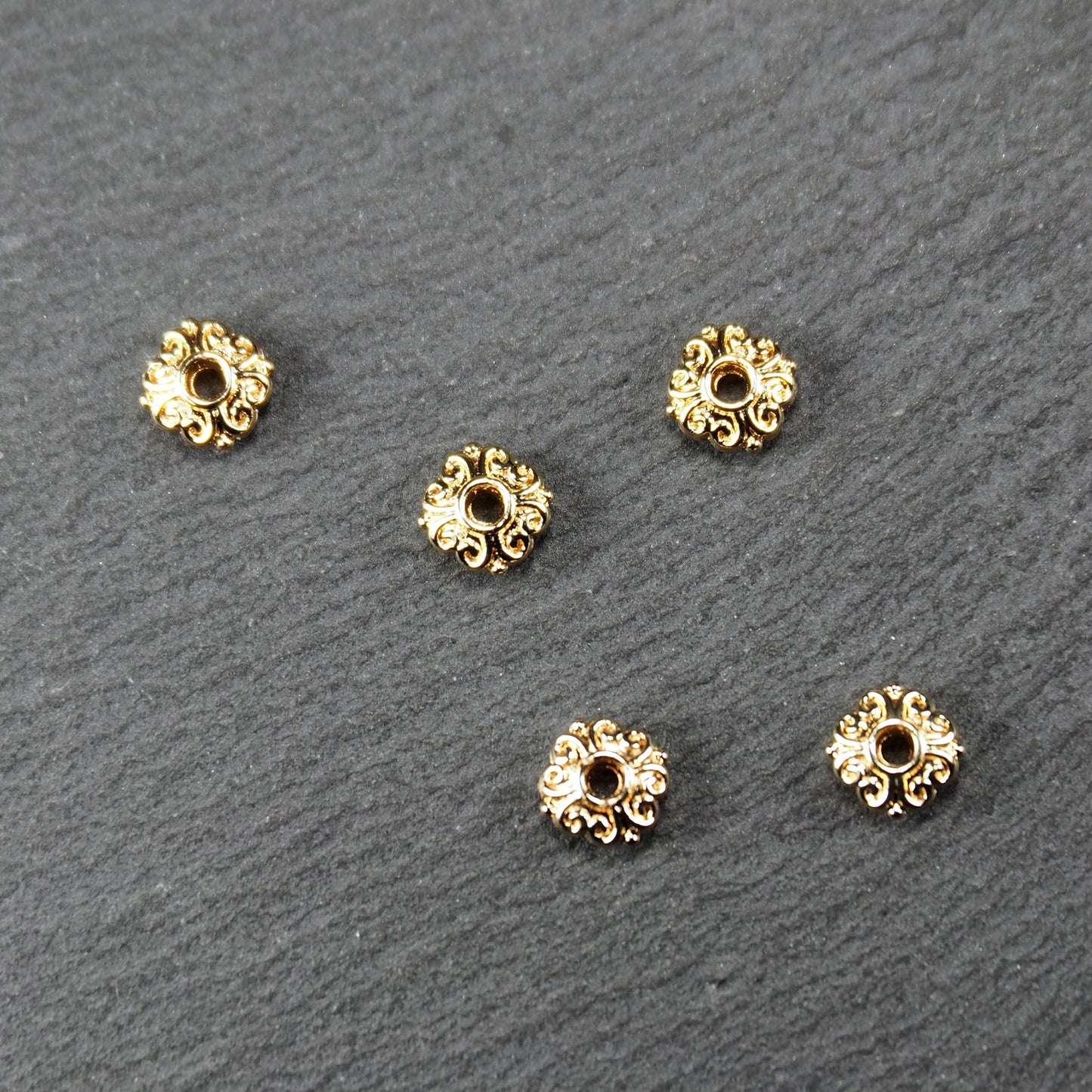 Runde goldfarbene Spacer Perlen mit glänzender Oberfläche, reliefartigem floralem Ornament und zentralem runden Durchbruch.