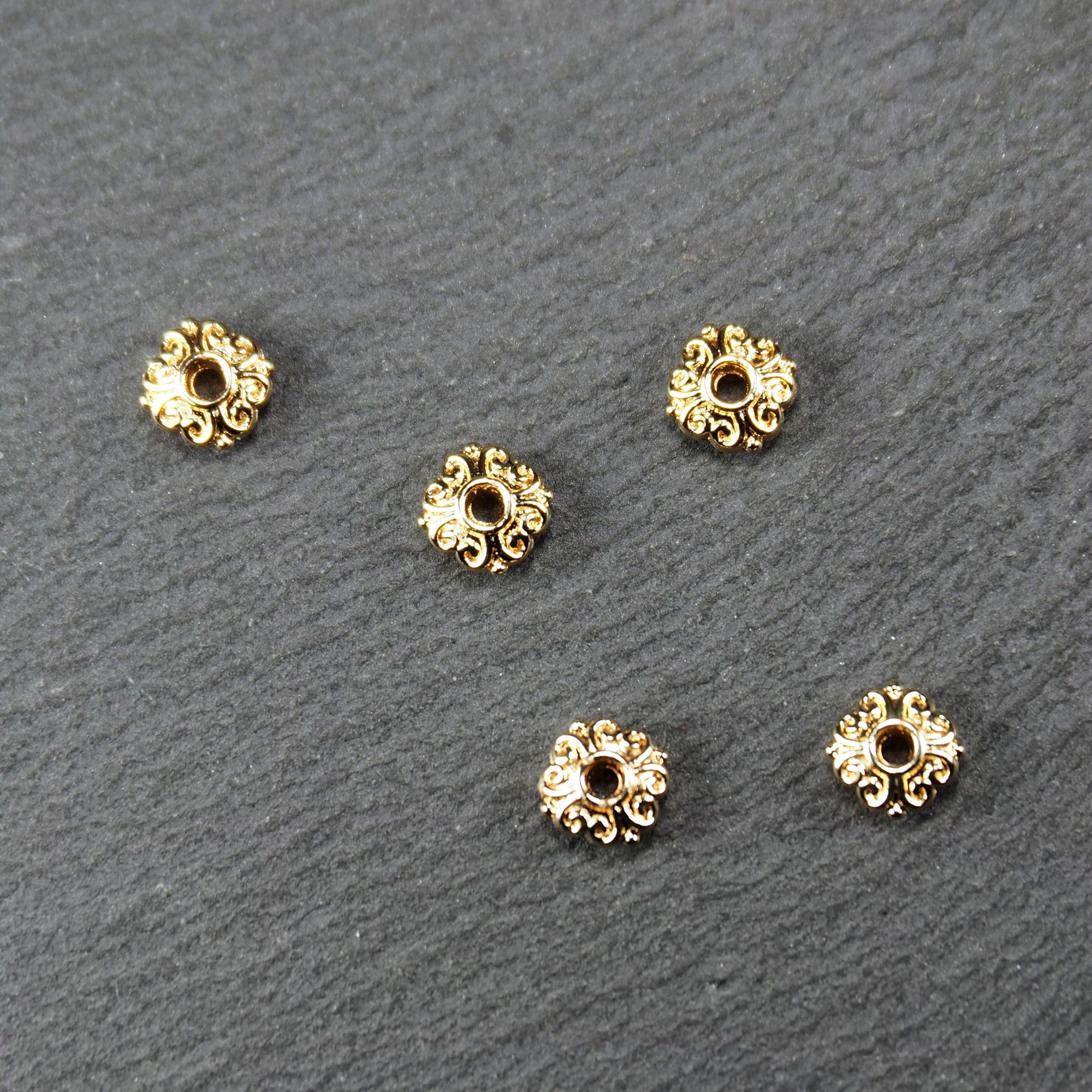 Runde goldfarbene Spacer Perlen mit glänzender Oberfläche, reliefartigem floralem Ornament und zentralem runden Durchbruch.