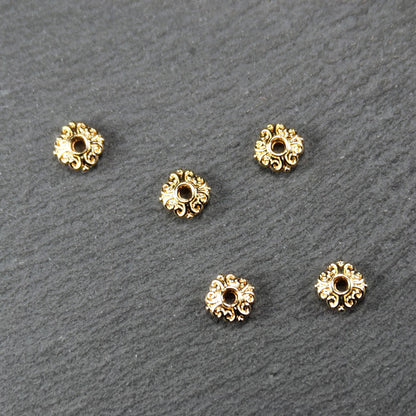 Runde goldfarbene Spacer Perlen mit glänzender Oberfläche, reliefartigem floralem Ornament und zentralem runden Durchbruch.