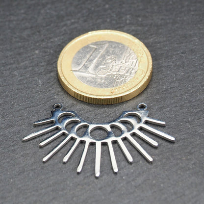 Versilberter Metallverbinder, halbkreisförmig und durchbrochen, mit rundem Mittelloch, mehreren schmalen radialen Strahlen, glänzender Oberfläche und zwei kleinen Ösen oben.