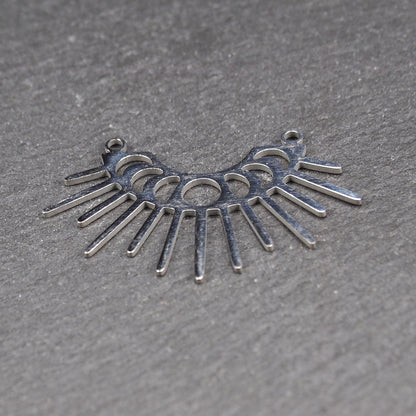 Versilberter Metallverbinder, halbkreisförmig und durchbrochen, mit rundem Mittelloch, mehreren schmalen radialen Strahlen, glänzender Oberfläche und zwei kleinen Ösen oben.