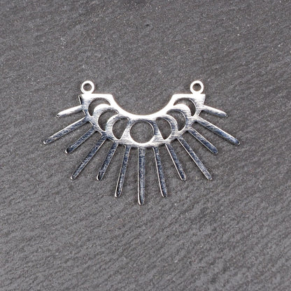 Versilberter Metallverbinder, halbkreisförmig und durchbrochen, mit rundem Mittelloch, mehreren schmalen radialen Strahlen, glänzender Oberfläche und zwei kleinen Ösen oben.
