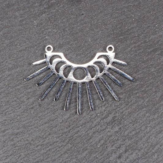 Versilberter Metallverbinder, halbkreisförmig und durchbrochen, mit rundem Mittelloch, mehreren schmalen radialen Strahlen, glänzender Oberfläche und zwei kleinen Ösen oben.