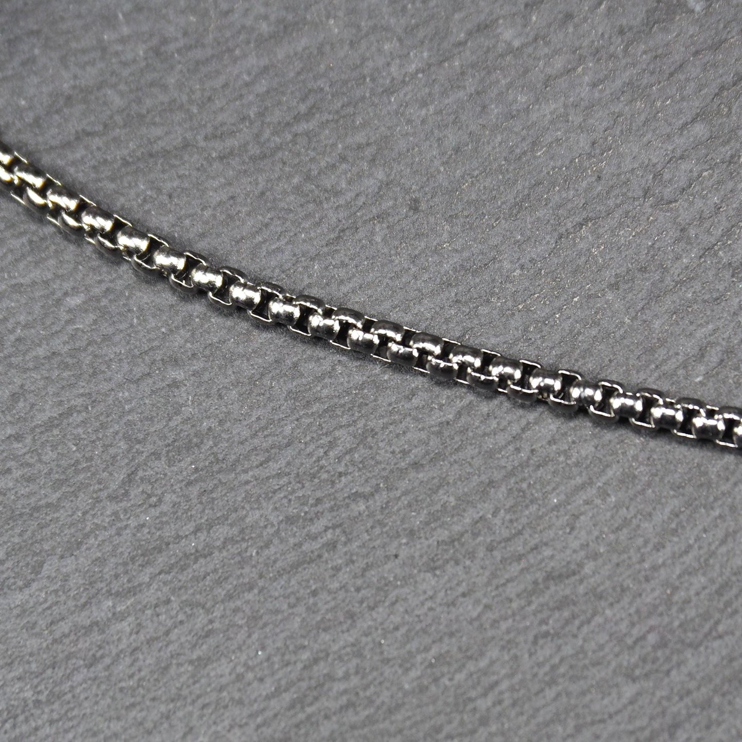 Quadratische Boxkette aus silberfarbenem, glänzendem Metall mit eng aneinandergereihten quadratischen Gliedern, diagonal gelegt.