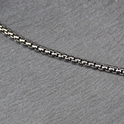 Quadratische Boxkette aus silberfarbenem, glänzendem Metall mit eng aneinandergereihten quadratischen Gliedern, diagonal gelegt.