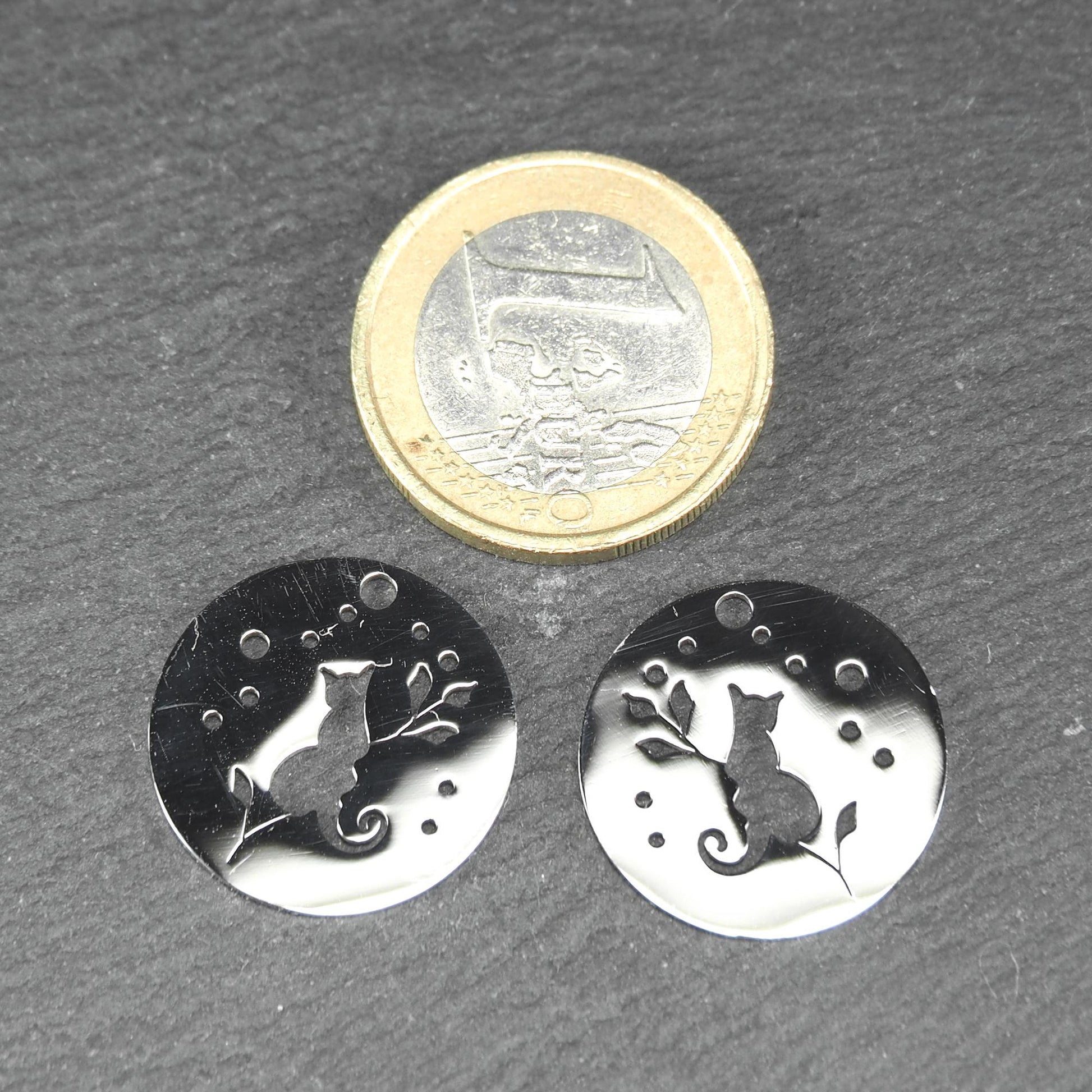 Runder, flacher Anhänger aus poliertem Edelstahl, Cut-out mit sitzender Katzen-Silhouette und Blattzweig, Öse oben und mehrere kleine Bohrungen.