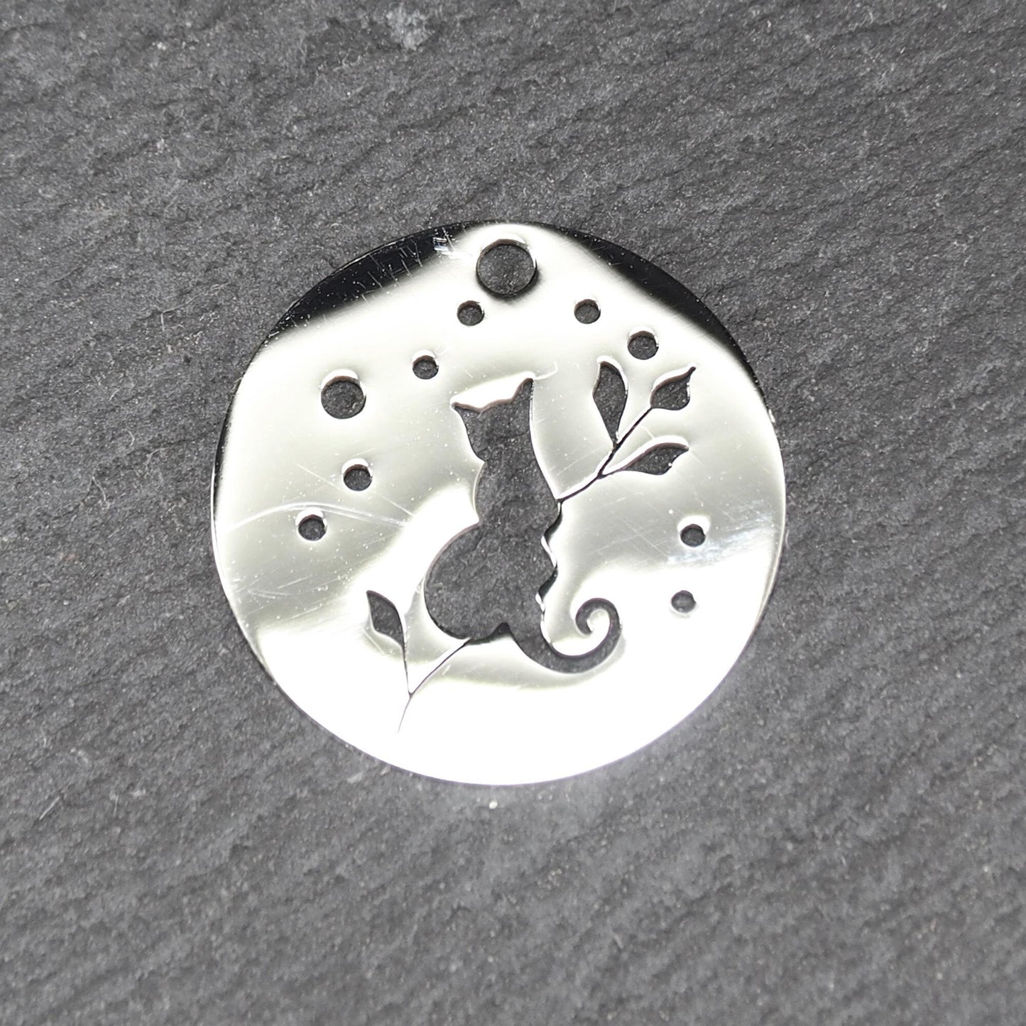 Runder, flacher Anhänger aus poliertem Edelstahl, Cut-out mit sitzender Katzen-Silhouette und Blattzweig, Öse oben und mehrere kleine Bohrungen.