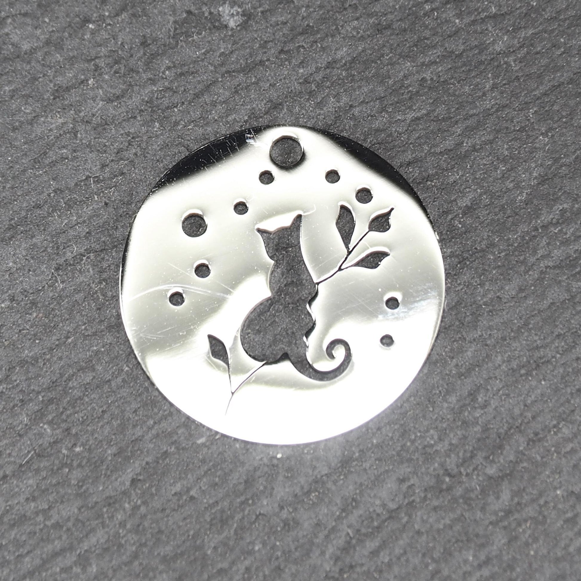 Runder, flacher Anhänger aus poliertem Edelstahl, Cut-out mit sitzender Katzen-Silhouette und Blattzweig, Öse oben und mehrere kleine Bohrungen.