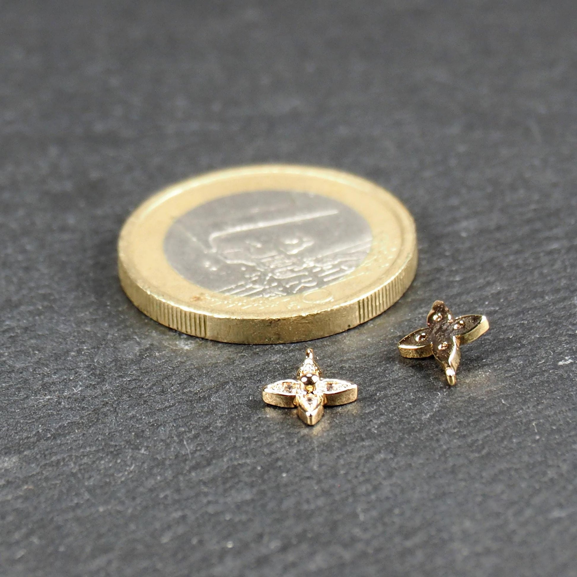 Vierblättriger goldfarbener Anhänger mit vier eingelassenen klaren Steinchen und zentraler Kugel, Öse sichtbar; daneben 1‑Euro‑Münze.