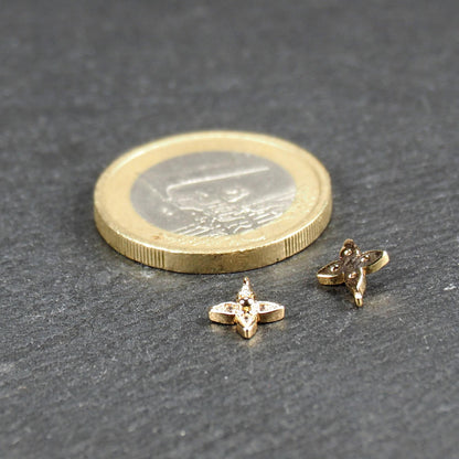 Vierblättriger goldfarbener Anhänger mit vier eingelassenen klaren Steinchen und zentraler Kugel, Öse sichtbar; daneben 1‑Euro‑Münze.