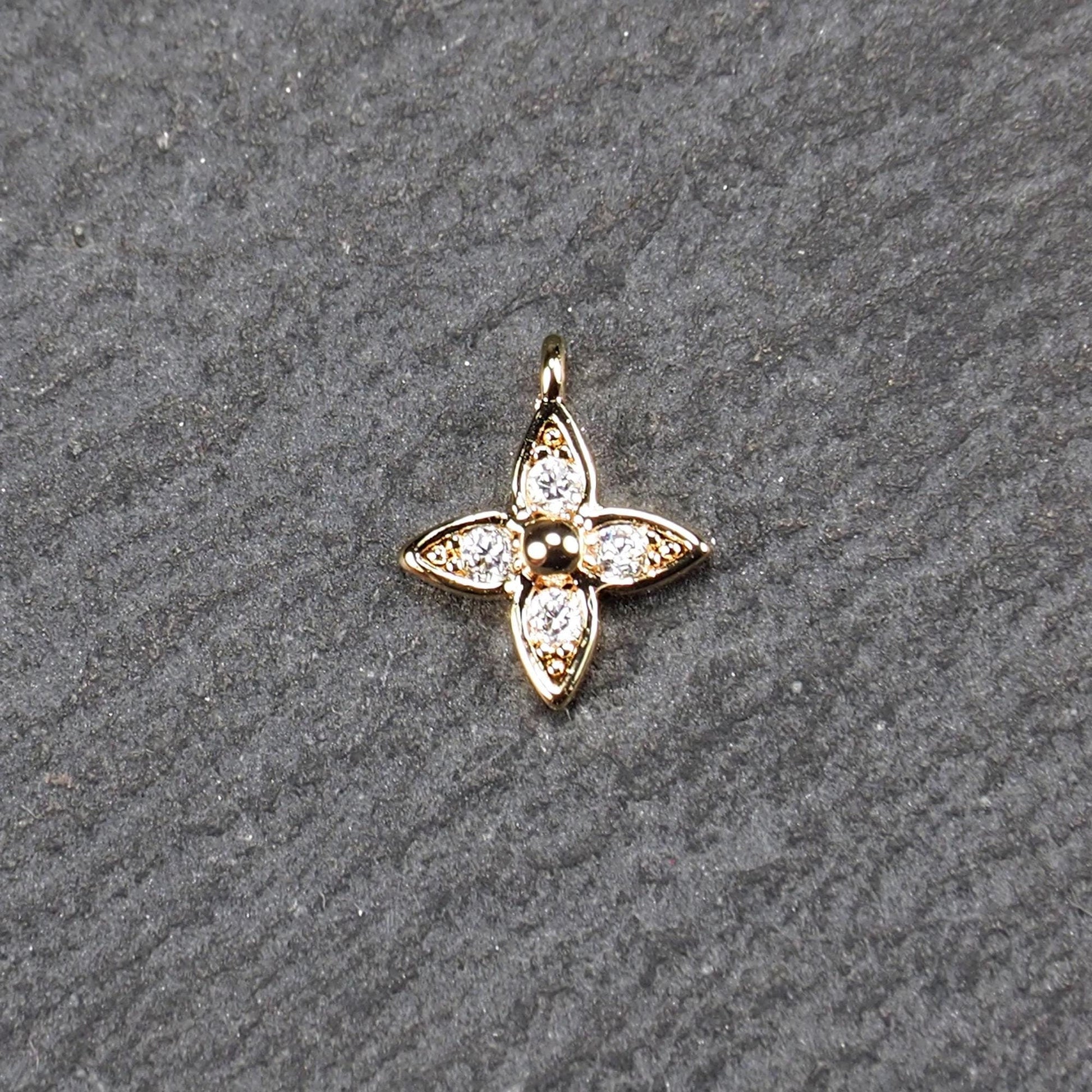Vierblättriger goldfarbener Blütenanhänger mit zentraler Kugel, vier eingesetzten Zirkonia in den Blattspitzen und oberer Öse.