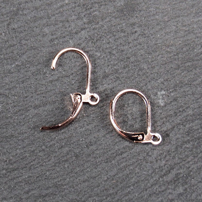 Zwei rosévergoldete Klappbrisuren in glänzender Metalloptik, ovale Leverback-Form mit sichtbarer kleinen Öse am unteren Ende, auf dunklem Hintergrund.