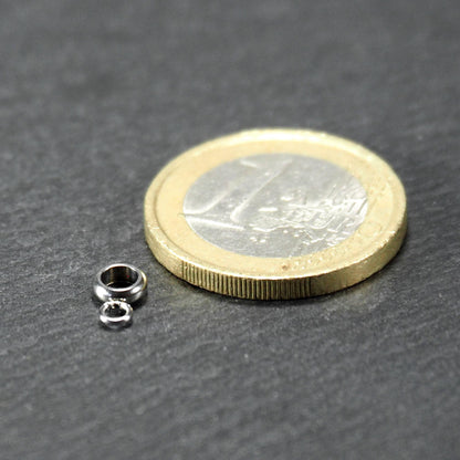 Kleine goldfarbene glänzende runde Anhängeröse in kompakter durchbrochener Ringform neben einer 1-Euro-Münze als Größenskalierung.