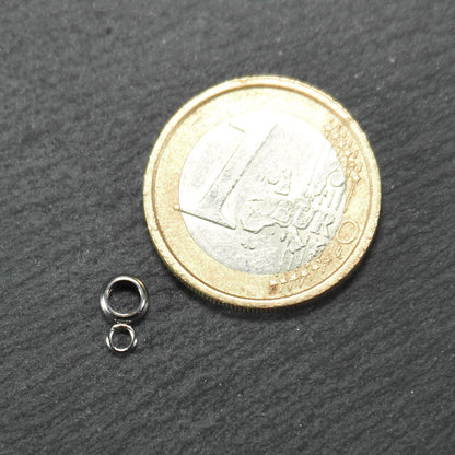 Kleine goldfarbene glänzende runde Anhängeröse in kompakter durchbrochener Ringform neben einer 1-Euro-Münze als Größenskalierung.