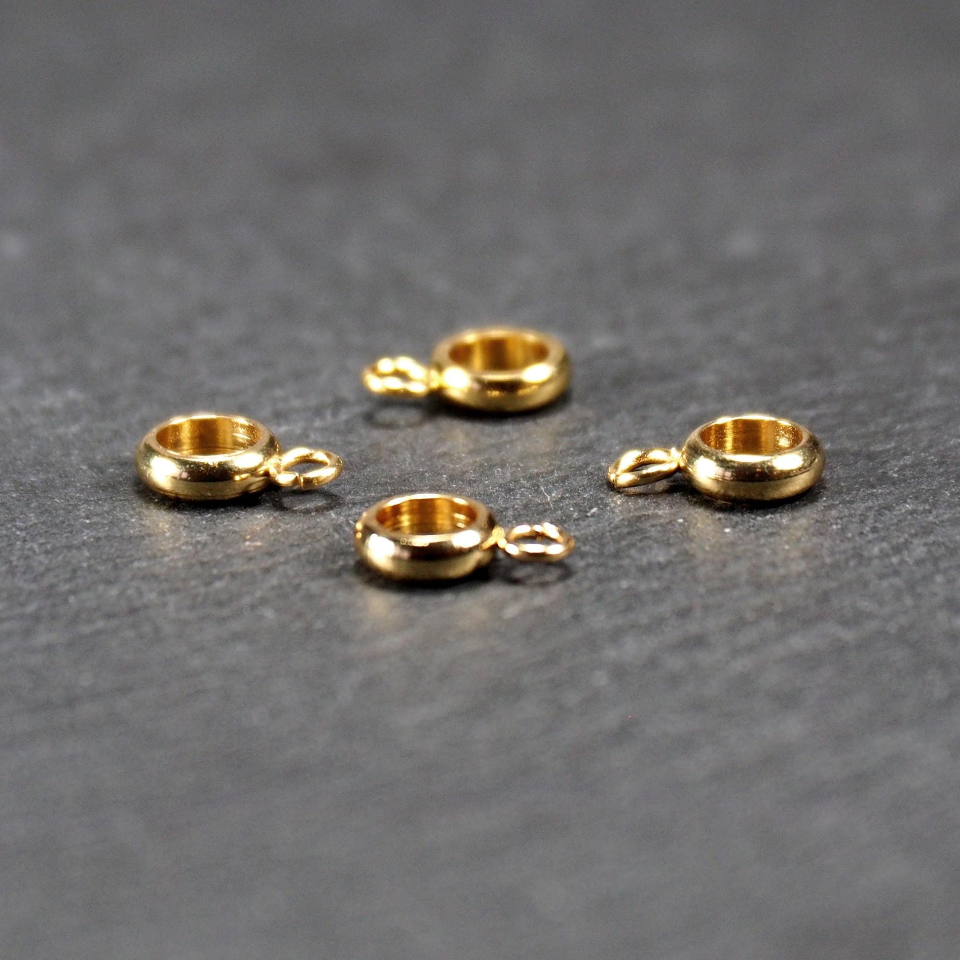 Vier vergoldete ringförmige Anhängerösen mit glänzender goldfarbener Oberfläche, hohlem Mittelring und jeweils kleinem seitlichem Ösenring.