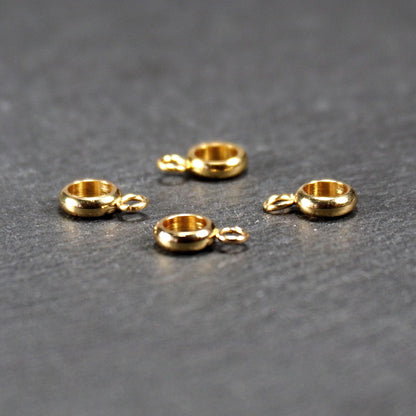 Vier vergoldete ringförmige Anhängerösen mit glänzender goldfarbener Oberfläche, hohlem Mittelring und jeweils kleinem seitlichem Ösenring.