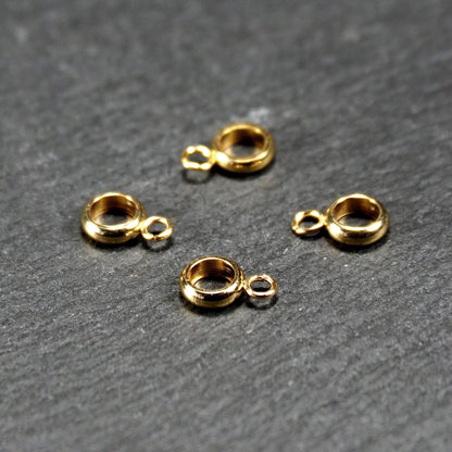 Vier vergoldete ringförmige Anhängerösen mit glänzender goldfarbener Oberfläche, hohlem Mittelring und jeweils kleinem seitlichem Ösenring.