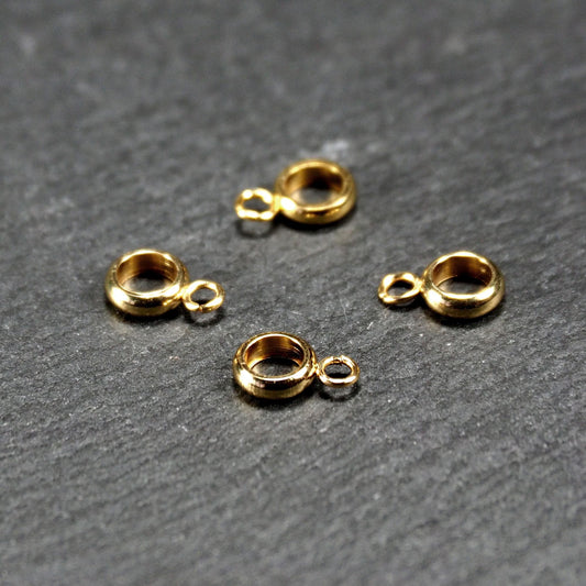 Vier vergoldete ringförmige Anhängerösen mit glänzender goldfarbener Oberfläche, hohlem Mittelring und jeweils kleinem seitlichem Ösenring.