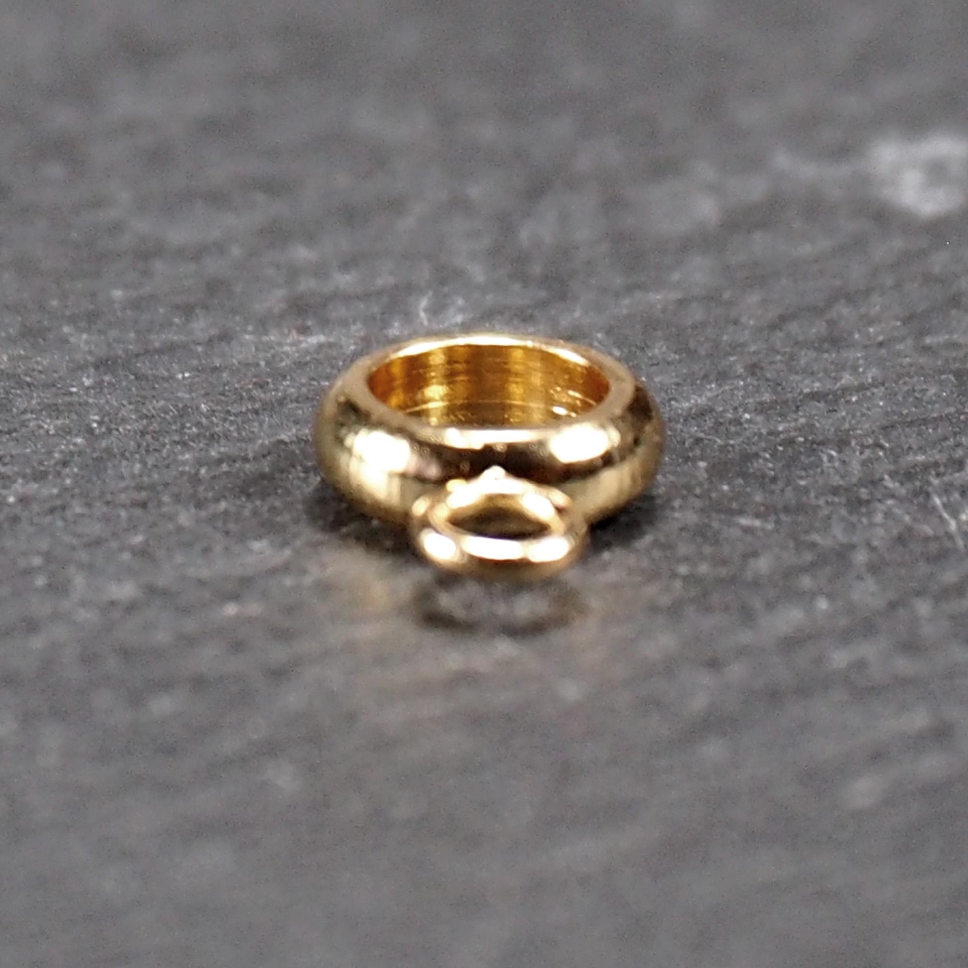 Ringförmige, glänzend goldfarbene Anhängeröse mit großem runden Loch und kleiner runder Anhängerschlaufe.