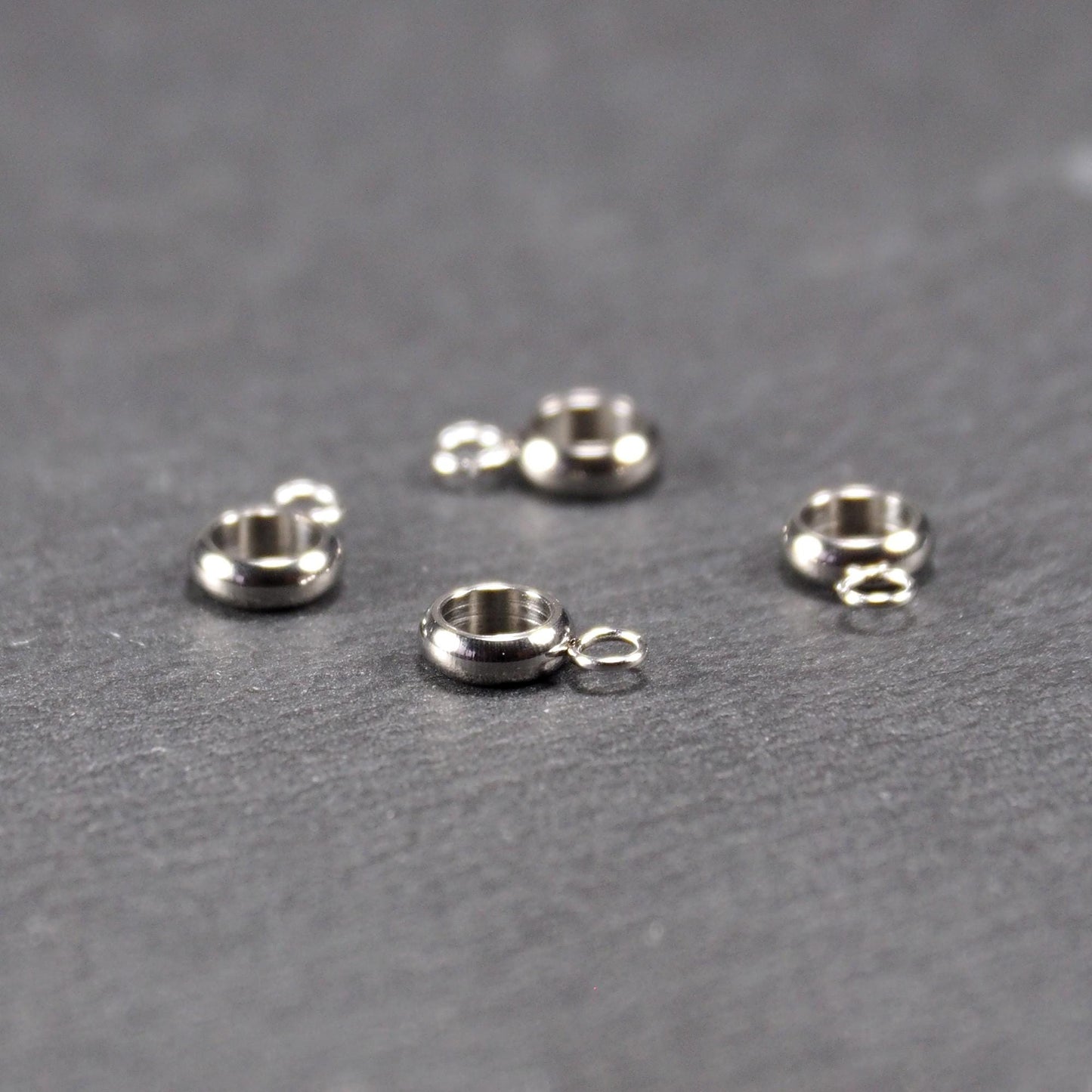 Vier glänzende silberfarbene runde Anhängerösen, jeweils ein größerer hohler Ring mit einer kleineren beweglichen Ringöse.