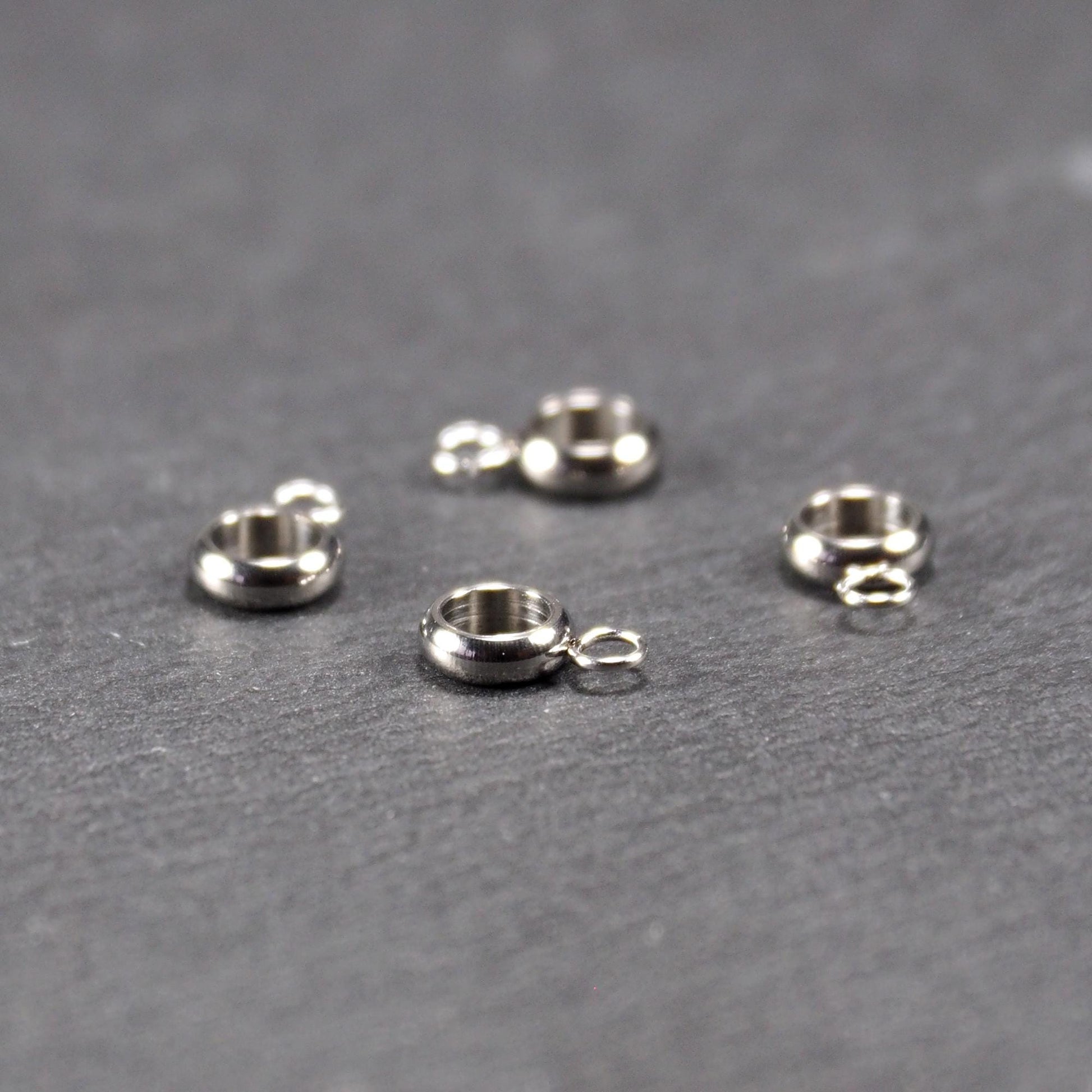 Vier glänzende silberfarbene runde Anhängerösen, jeweils ein größerer hohler Ring mit einer kleineren beweglichen Ringöse.