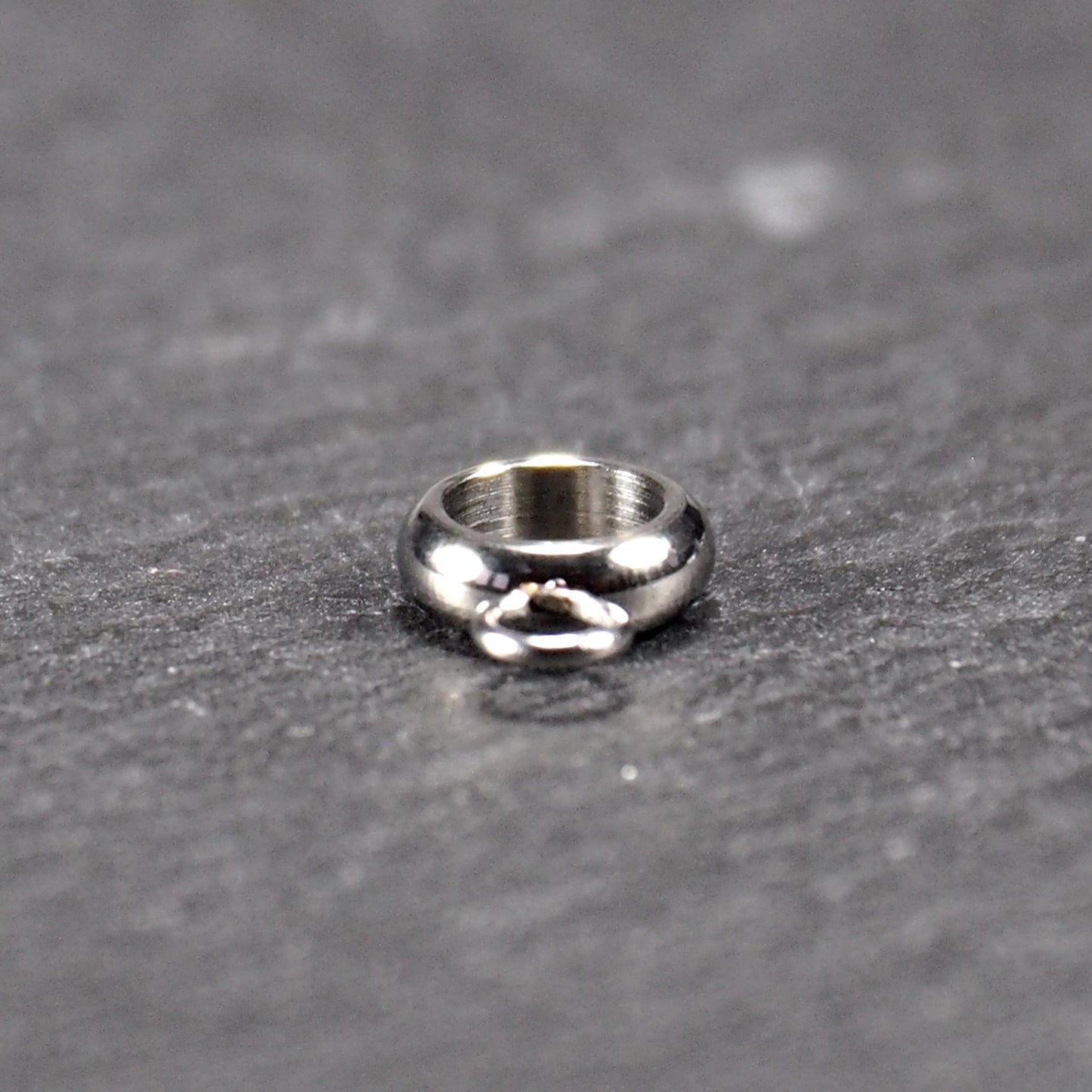 Anhängeröse, silberfarbene glänzende Metallrundung mit zentraler Öffnung und einer kleineren beweglichen Ringöse als Verbindungselement.