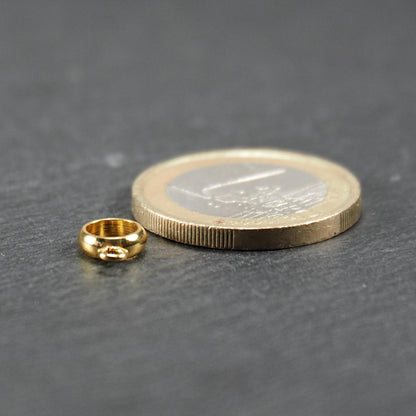 Runde goldfarbene glänzende Anhängeröse mit integriertem kleinem Ösenring neben einer 1‑Euro‑Münze zum Größenvergleich.