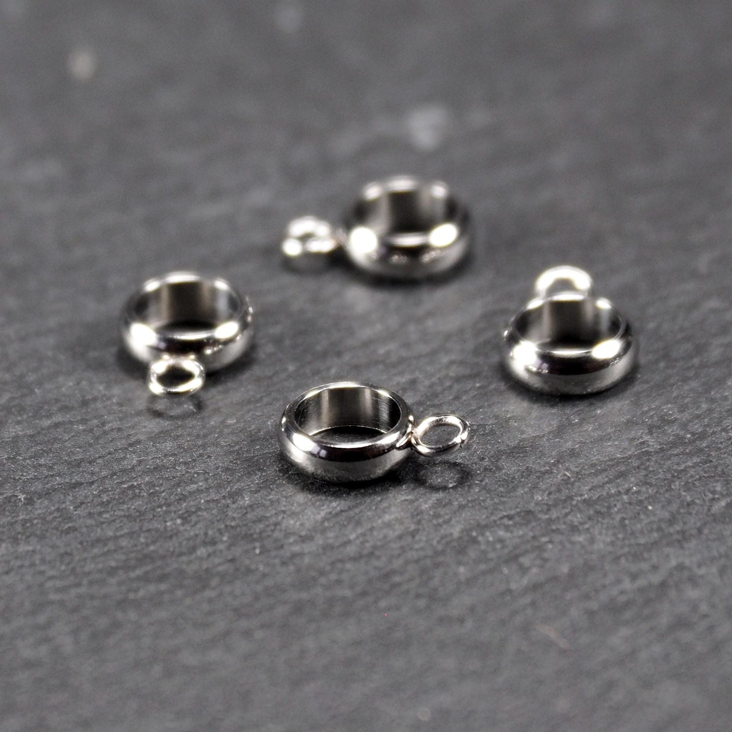 Vier runde, silberfarbene Anhängerösen mit glänzender Oberfläche: hohle Ringscheiben mit jeweils einer kleinen Öse.