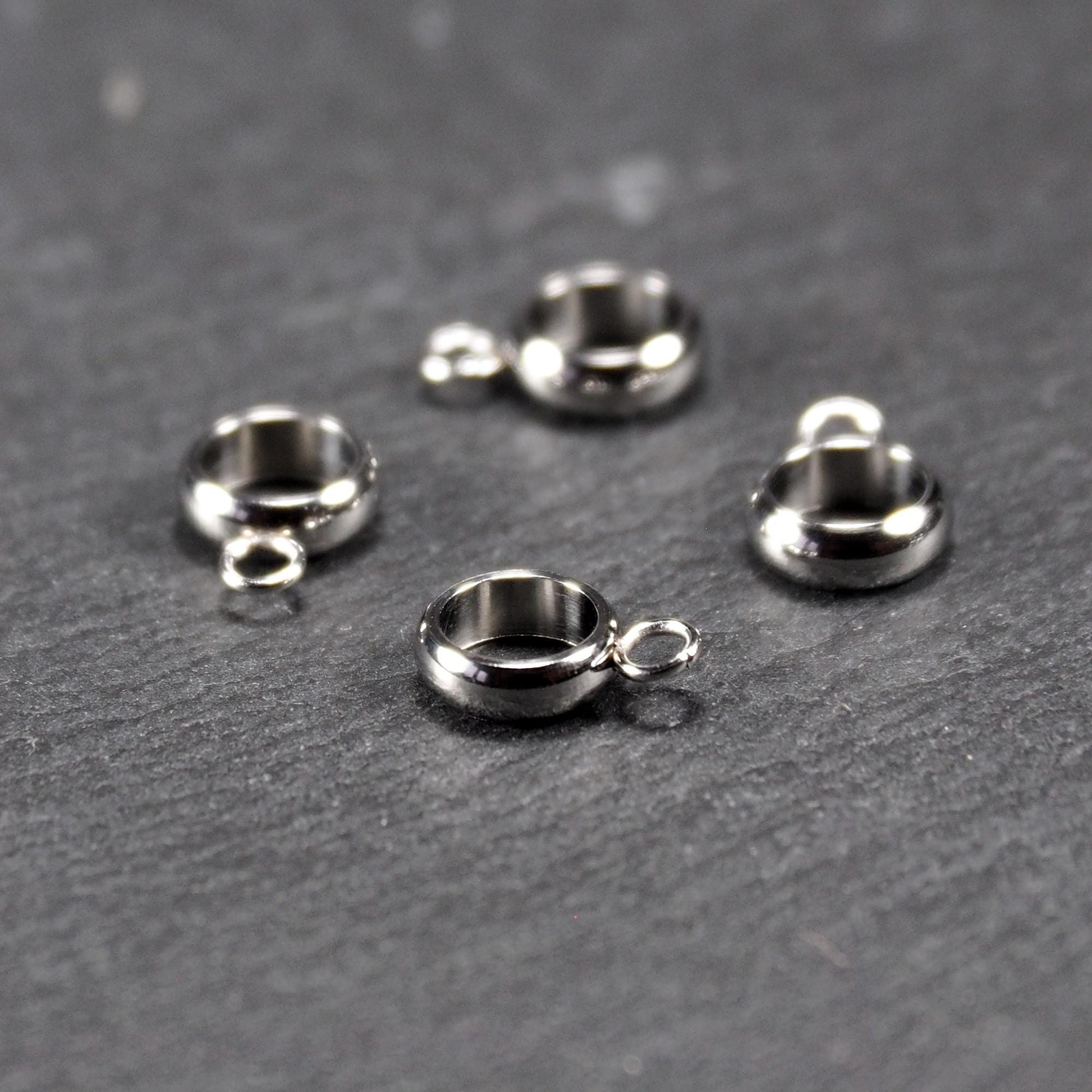 Vier runde, silberfarbene Anhängerösen mit glänzender Oberfläche: hohle Ringscheiben mit jeweils einer kleinen Öse.