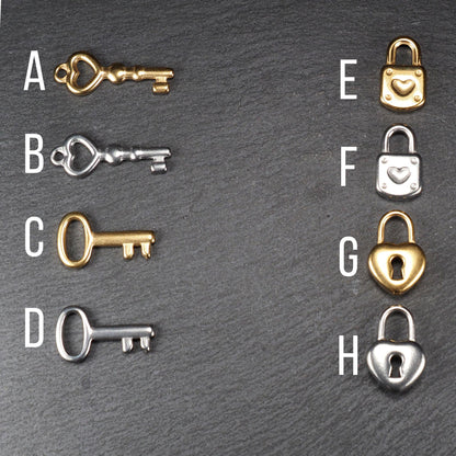 Acht Metallanhänger (Schlüssel und Schlösser), silber- oder goldfarben, glatte Oberfläche; Schlüssel mit herz- oder ovaler Öse, Schlösser quadratisch oder herzförmig mit Bügel.