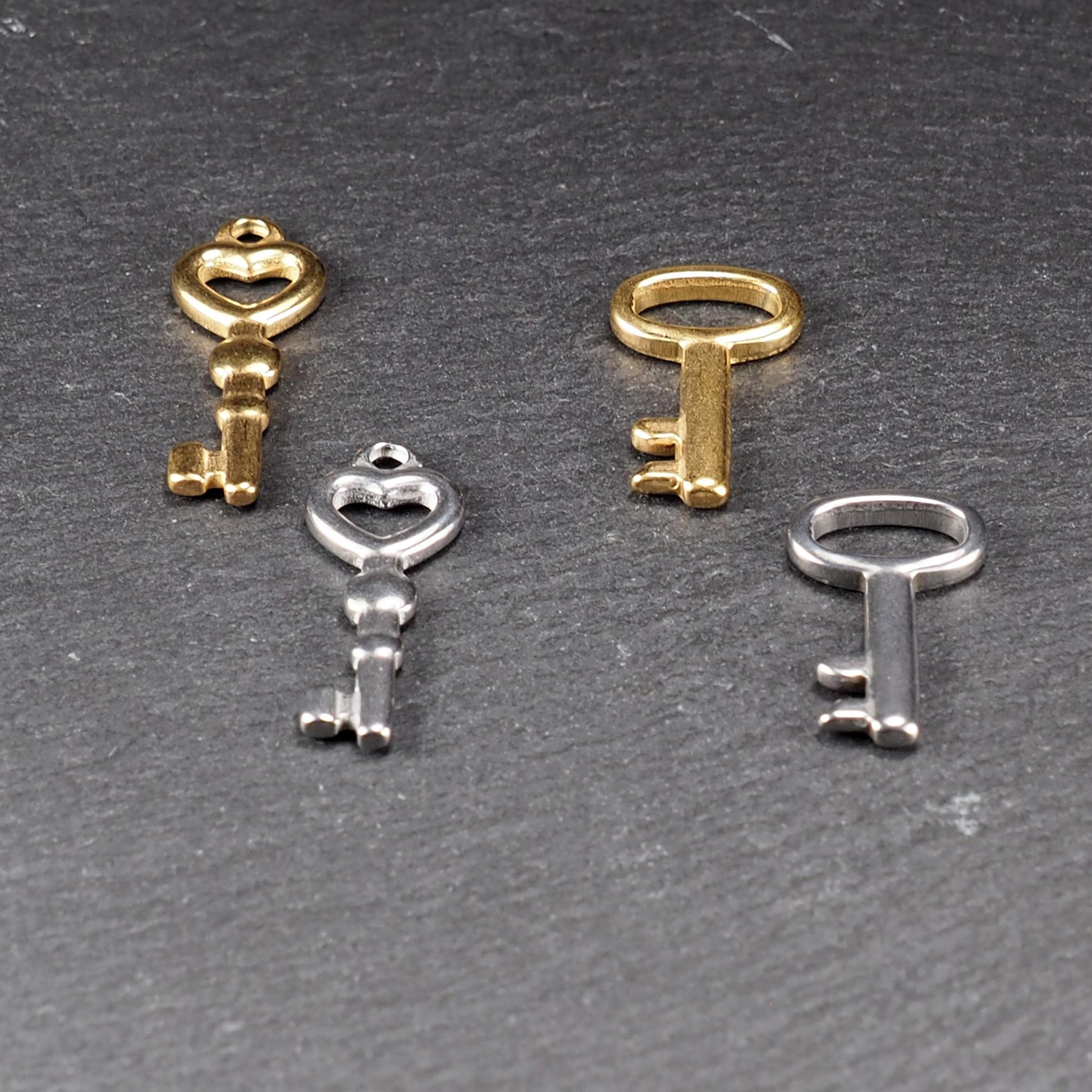 Vier glänzende Schlüsselanhänger, zwei vergoldet und zwei silberfarben; zwei mit herzförmiger Öse, zwei mit ovaler Öse.