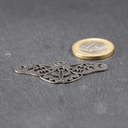 Anhänger / Verbinder in Mottenform aus poliertem silberfarbenem Edelstahl, filigranes durchbrochenes Ornament-Flügeldesign mit integrierter Öse oben. Neben einer 1 Euro Münze zum Größenvergleich.