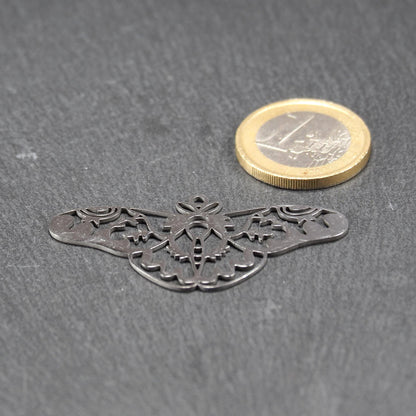 Anhänger / Verbinder in Mottenform aus poliertem silberfarbenem Edelstahl, filigranes durchbrochenes Ornament-Flügeldesign mit integrierter Öse oben. Neben einer 1 Euro Münze zum Größenvergleich.