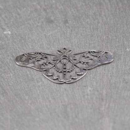 Anhänger / Verbinder in Mottenform aus poliertem silberfarbenem Edelstahl, filigranes durchbrochenes Ornament-Flügeldesign mit integrierter Öse oben.