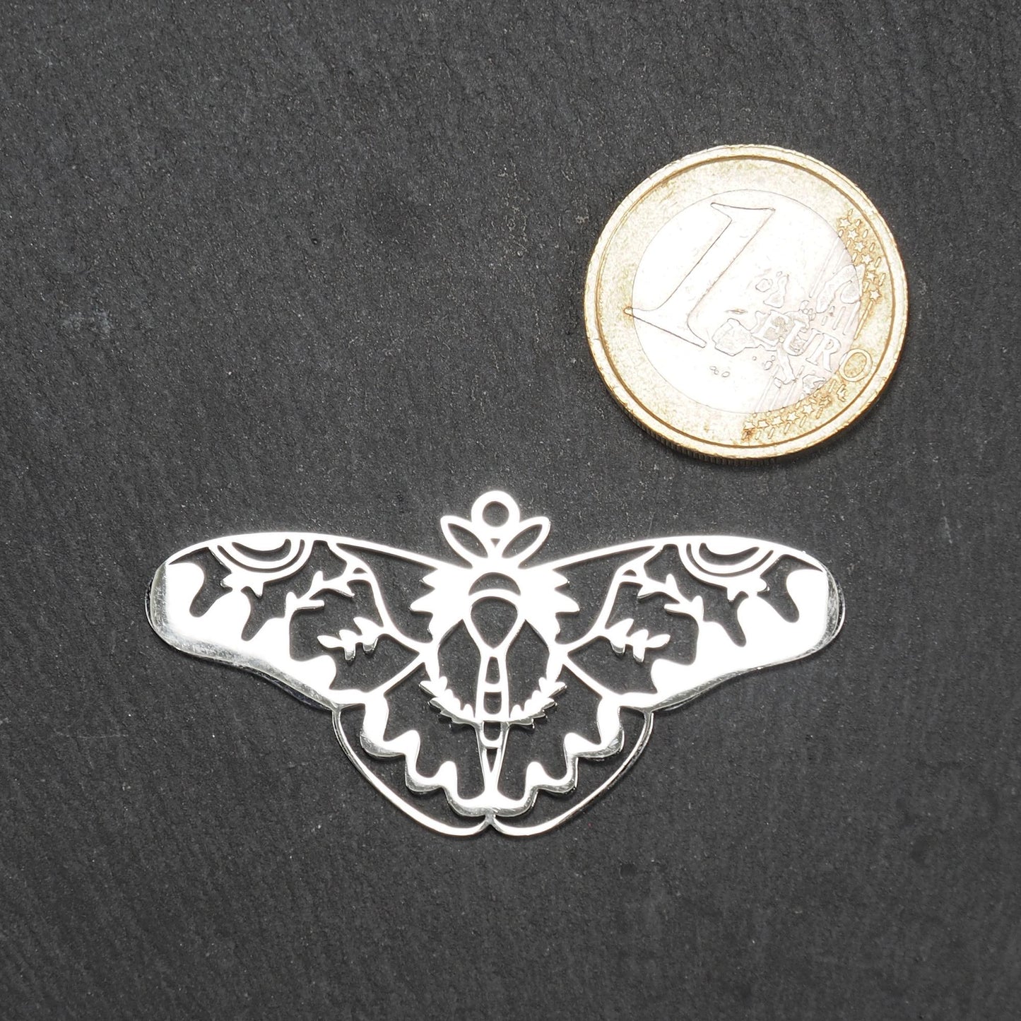 Anhänger / Verbinder in Mottenform aus poliertem silberfarbenem Edelstahl, filigranes durchbrochenes Ornament-Flügeldesign mit integrierter Öse oben.