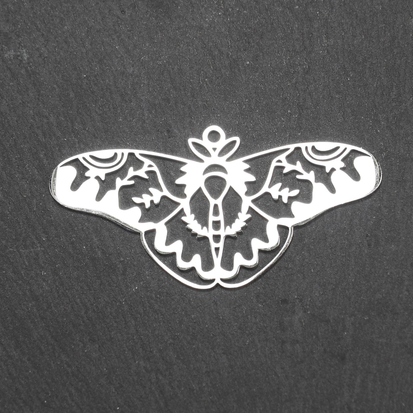 Anhänger / Verbinder in Mottenform aus poliertem silberfarbenem Edelstahl, filigranes durchbrochenes Ornament-Flügeldesign mit integrierter Öse oben.