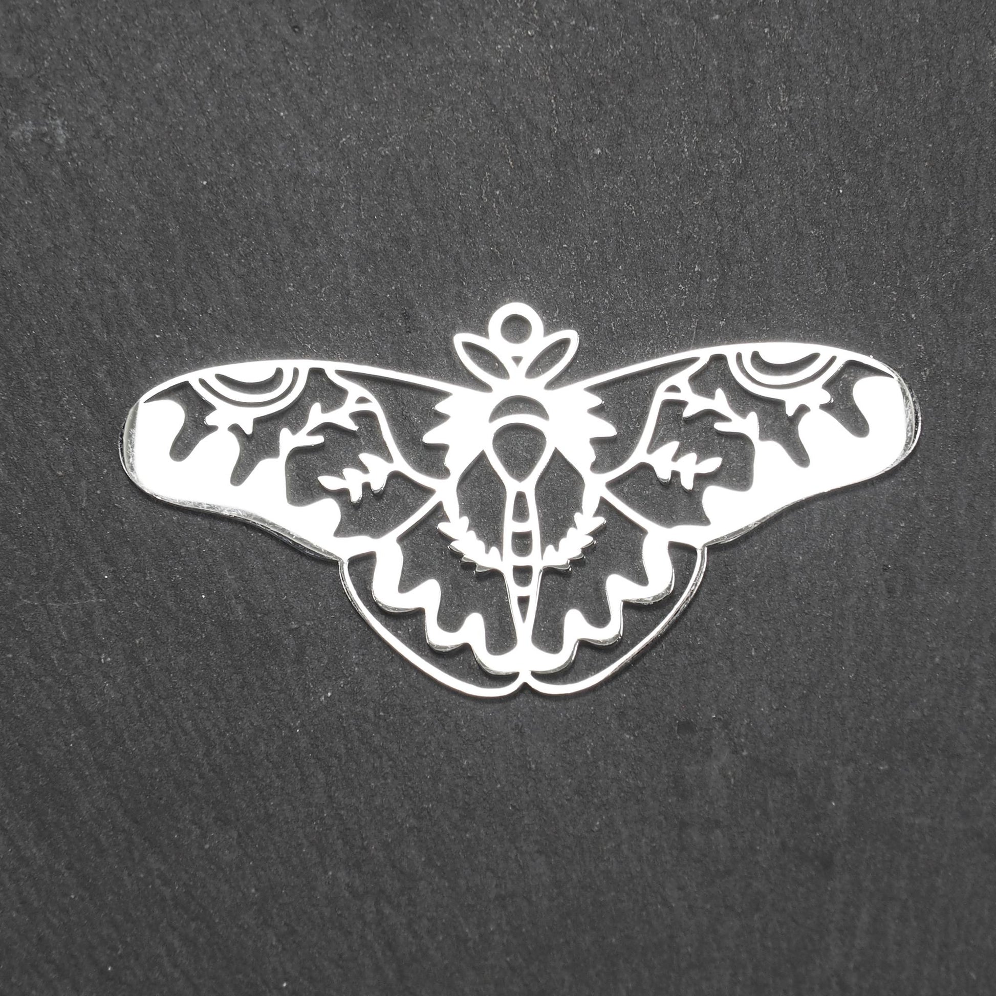 Anhänger / Verbinder in Mottenform aus poliertem silberfarbenem Edelstahl, filigranes durchbrochenes Ornament-Flügeldesign mit integrierter Öse oben.