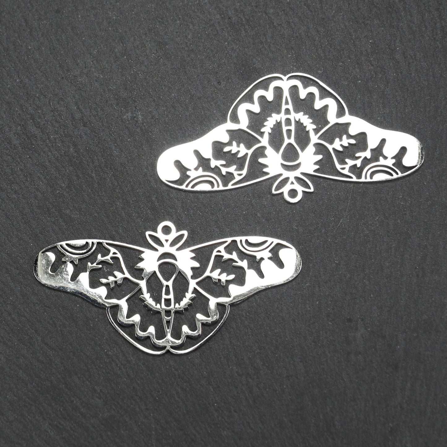 Anhänger / Verbinder in Mottenform aus poliertem silberfarbenem Edelstahl, filigranes durchbrochenes Ornament-Flügeldesign mit integrierter Öse oben.