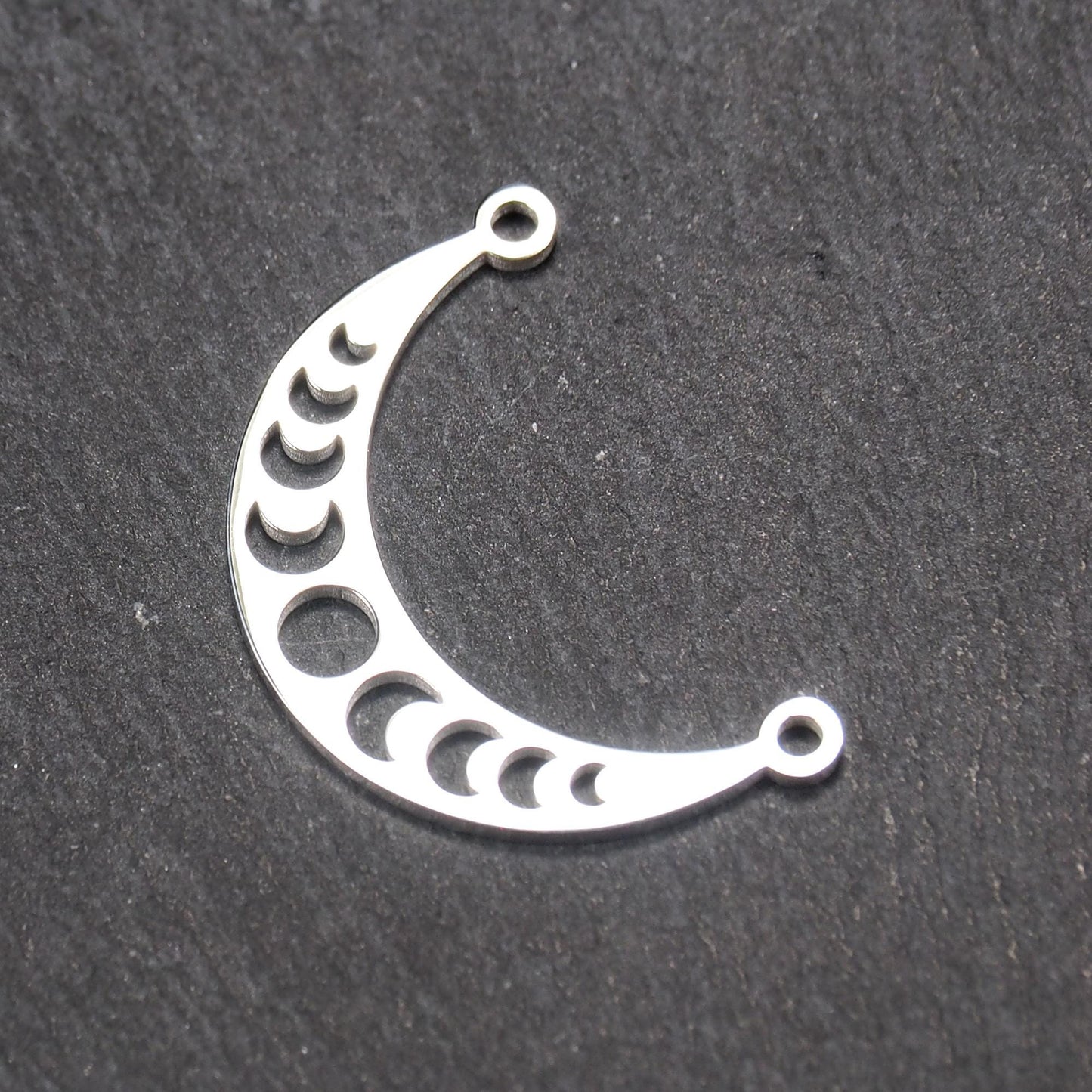 Sichelförmiger silberner Metallverbinder mit ausgeschnittenem Mondphasen-Motiv und je einer Rundöse an den Enden.