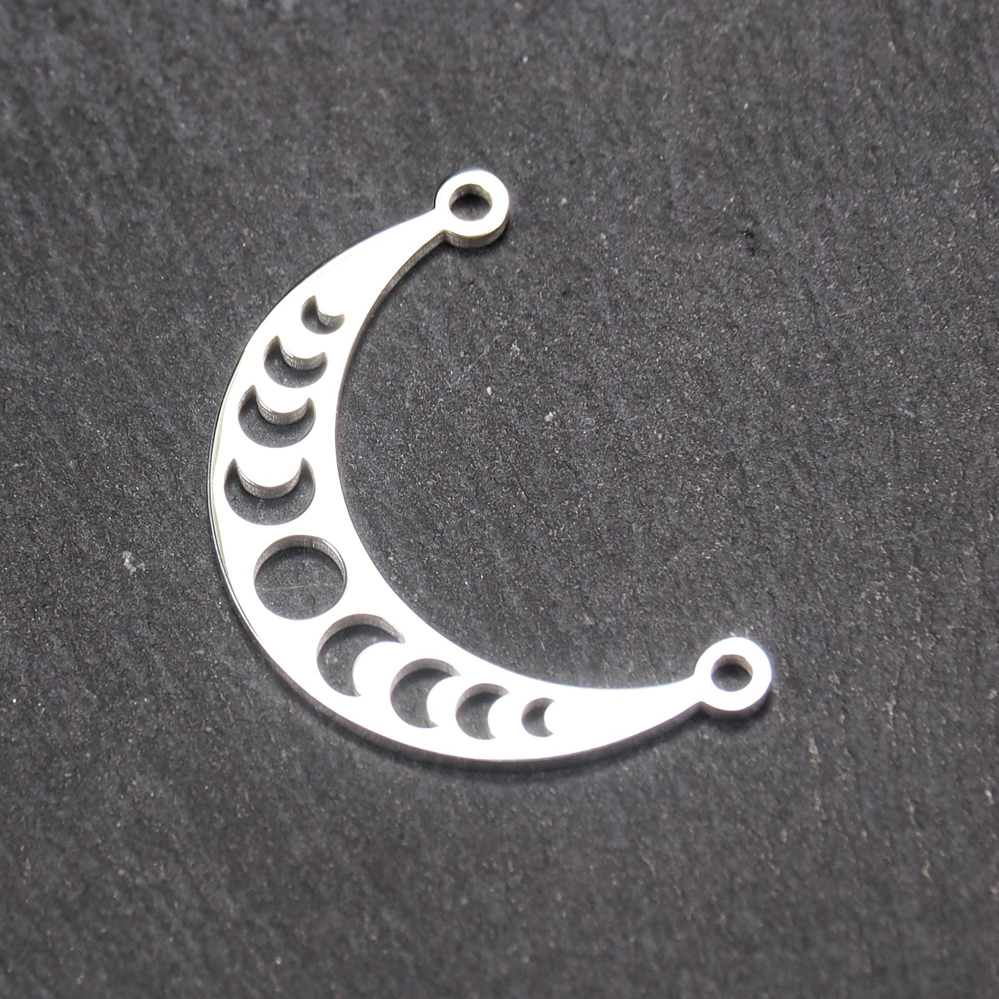 Sichelförmiger silberner Metallverbinder mit ausgeschnittenem Mondphasen-Motiv und je einer Rundöse an den Enden.