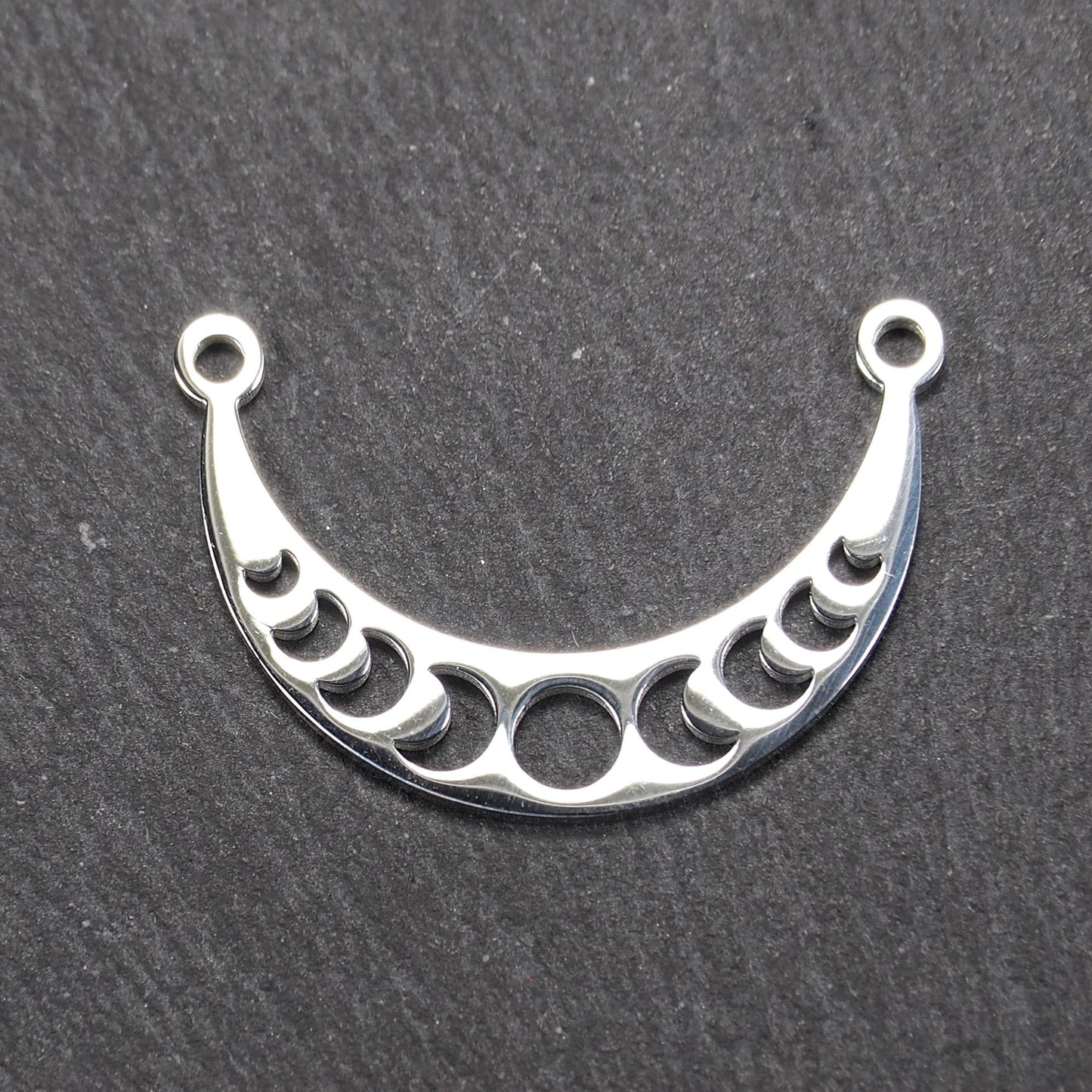 Sichelförmiger silberner Metallverbinder mit ausgeschnittenem Mondphasen-Motiv und je einer Rundöse an den Enden.