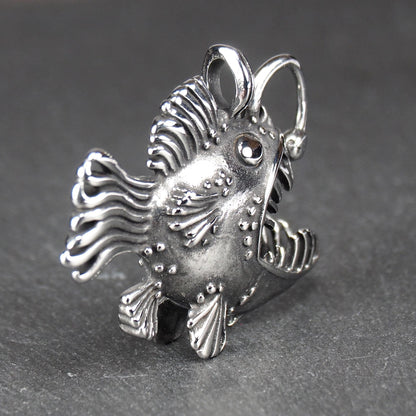 3D-Anhänger Anglerfisch, silberglänzend, mit geöffnetem Maul und dolchartigen Zähnen, geriffelten Flossen, punktiertem Körper und Öse.