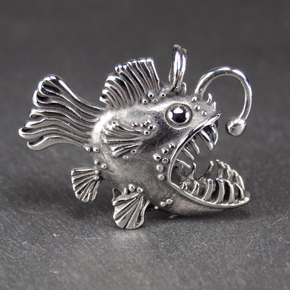 3D-Anhänger Anglerfisch, silberglänzend, mit geöffnetem Maul und dolchartigen Zähnen, geriffelten Flossen, punktiertem Körper und Öse.