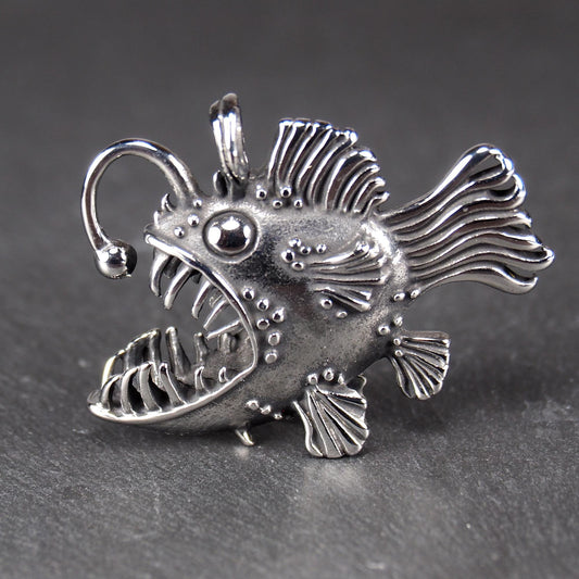 3D-Anhänger Anglerfisch, silberglänzend, mit geöffnetem Maul und dolchartigen Zähnen, geriffelten Flossen, punktiertem Körper und Öse.