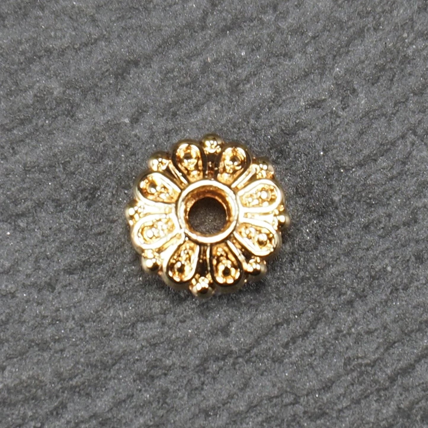 Runde, goldfarbene Scheiben-Spacer-Perle mit mittigem Loch und reliefierter, blütenartiger radialer Ornamentgravur.
