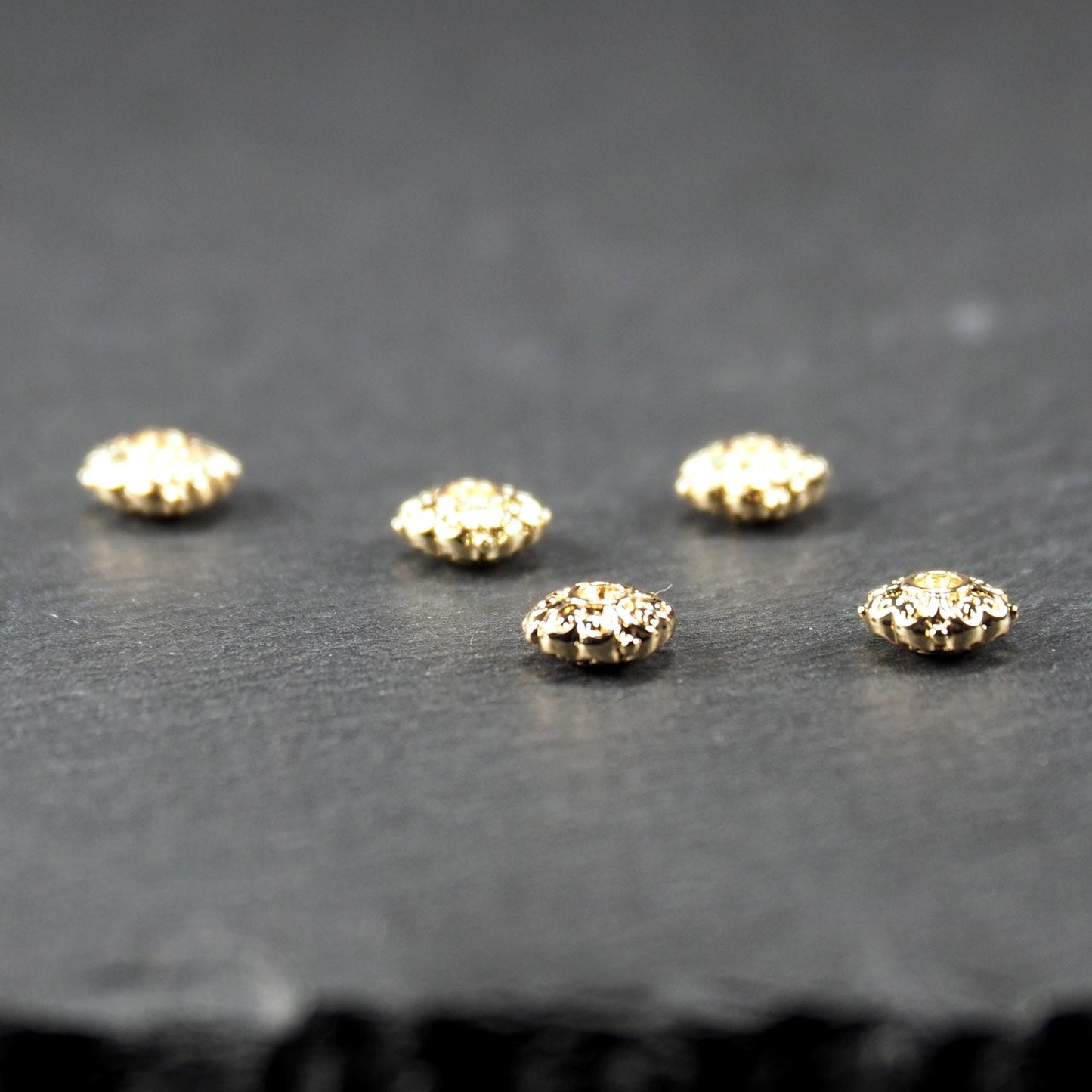Runde goldfarbene Spacer Perlen mit glänzender Oberfläche, reliefartigem floralem Ornament und zentralem runden Durchbruch.